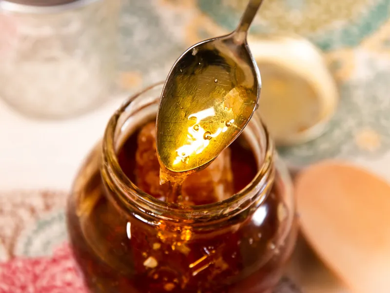 A spoon lifting golden honey from an open jar